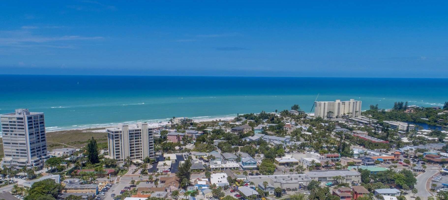 A coastal cityscape with high-rise buildings, a beach, and a clear blue sky.