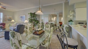 Ein geräumiges Wohnzimmer mit einem Glastisch, einer gestreiften Couch und einem Essbereich mit Stühlen und einem Tisch.