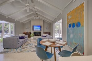 Uma sala de estar espaçosa com lareira, uma TV grande e um espaço de jantar com cadeiras azuis.