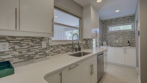 A modern kitchen with a large window, a built-in sink, and a stone backsplash. - Majestic Coastal Escape (Siesta Key)