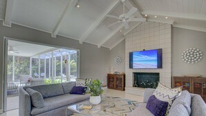 A spacious living room with a large TV, a fireplace, and a ceiling fan. - Majestic Coastal Escape (Siesta Key)