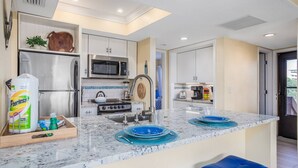 A modern kitchen with stainless steel appliances, a marble countertop, and a view to the outside. - Midnight Cove II Bldg 7: Top Floor With Views (Siesta Key)