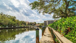 A wooden boardwalk over calm water, flanked by lush greenery and buildings in the background. - Midnight Cove II Bldg 7: Top Floor With Views (Siesta Key)