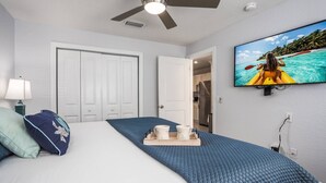 Een hotelkamer met een bed, een plafondventilator, een televisie aan de muur en een deur naar de keuken.