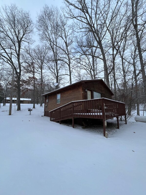 A wooden cabin with a deck, surrounded by snow-covered ground and leafless trees. - Patoka Lake One Bedroom Cozy #23 at Patoka 4 Seasons Resort (Eckerty)