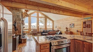 A log cabin with a stone fireplace, wooden dining table, and a kitchen with a gas stove. - Welcome to Lucky Us Cabin! Private + Close to Town (Breckenridge)