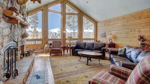 A cozy cabin interior with a stone fireplace, large windows offering mountain views, and a mix of leather and plaid furniture. - Welcome to Lucky Us Cabin! Private + Close to Town (Breckenridge)