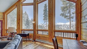 A cozy cabin interior with large windows offering a mountain view, a wooden dining table, and a comfortable seating area. - Welcome to Lucky Us Cabin! Private + Close to Town (Breckenridge)