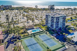 An aerial view of a hotel with multiple tennis courts, a pool, and a beach view.