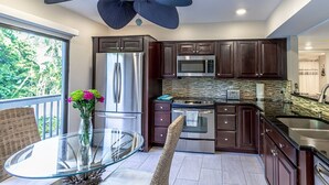 A modern kitchen with dark wood cabinets, stainless steel appliances, and a glass-top dining table. - Our House at the Beach Lakeside (Siesta Key)