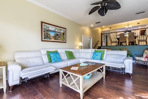 A living room with a white sofa, a wooden coffee table, and a painting of a tropical scene.
