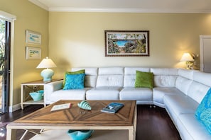 A living room with a white sofa, a coffee table, and two side tables with lamps. There are two framed pictures on the wall and a painting above the sofa.