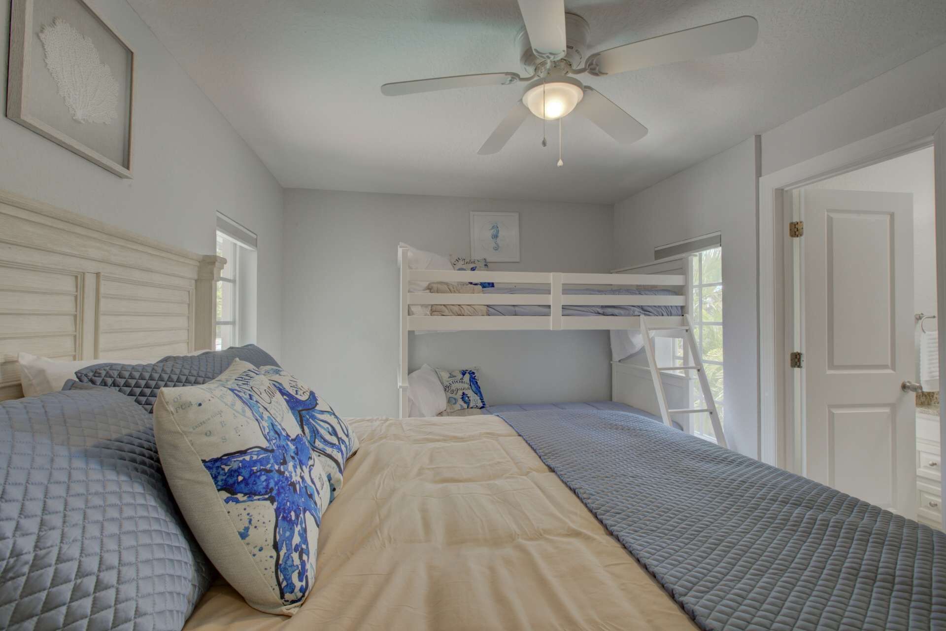 Une chambre avec des lits superposés, un ventilateur de plafond et une porte sur le côté droit.