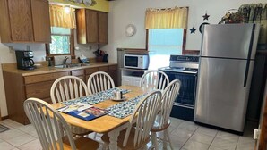 Una cocina con una mesa de madera, sillas blancas, un refrigerador, un microondas y un horno.
