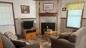 Una sala de estar con dos sofás, un televisor sobre un mueble de madera, una chimenea y un piso con diseño de piedra.