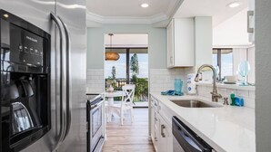 Una cocina moderna con electrodomésticos de acero inoxidable, un comedor con mesa y sillas blancas, y vistas al exterior.