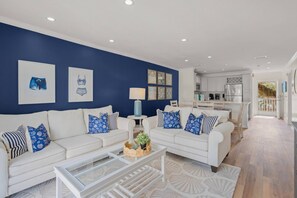 Uma sala de estar moderna com uma parede azul de destaque, sofás brancos e uma mesa de centro de vidro.