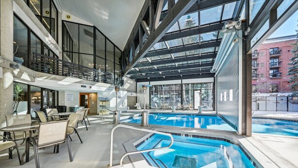 An indoor swimming pool with clear glass walls, a mezzanine level, and seating areas.