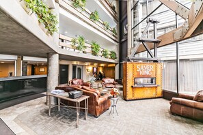 A hotel lobby with leather seating, a fireplace, and plants on balconies.