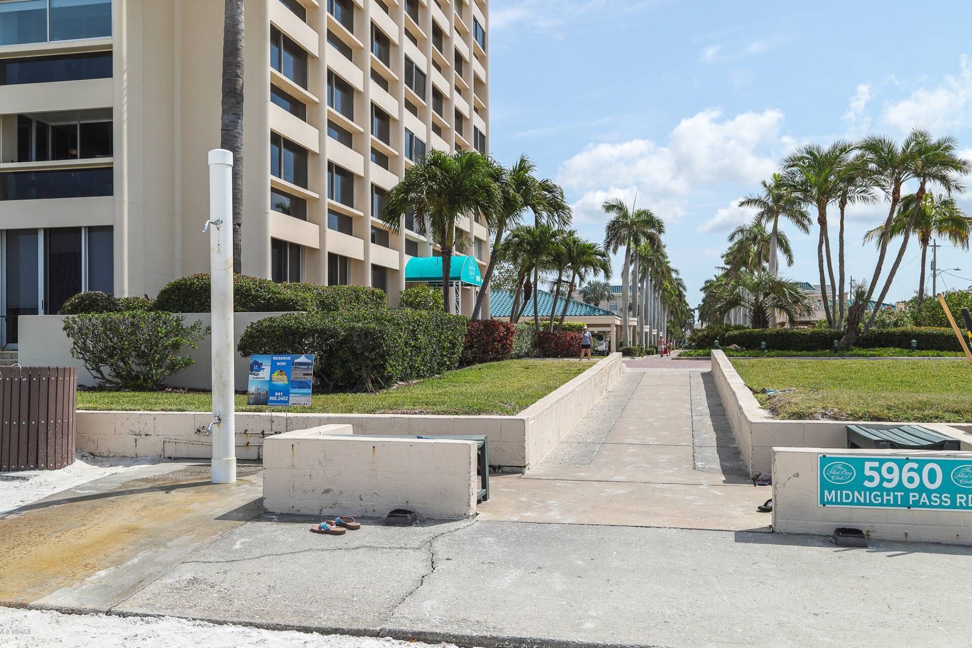 A mid-rise hotel with a modern facade, a paved walkway, and palm trees.