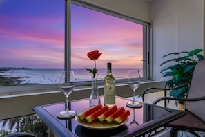 A balcony with a table set for two, featuring a bottle of wine, a rose, and a plate of watermelon slices. - Palm Bay Club 7th-floor Oceanfront Condo on Private Beach (Siesta Key)