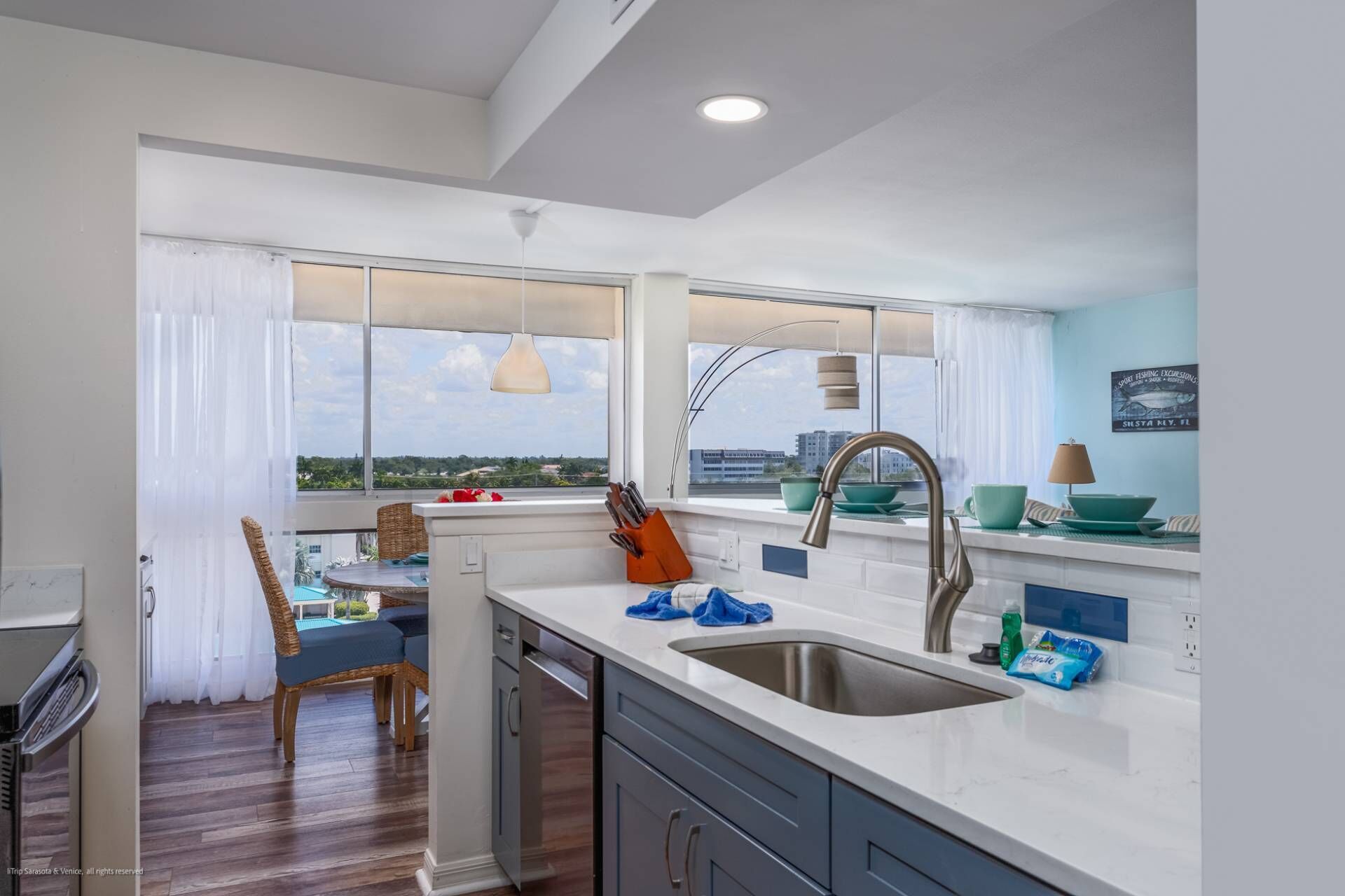 A modern kitchen with a large window, a dining area with a table and chairs, and a view of the cityscape.