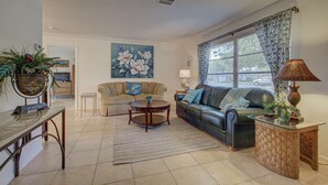 A living room with a sofa, a coffee table, a TV, and a large window with patterned curtains. - Peaceful Egret Pool Home in Venice (Venice)