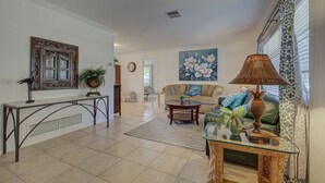 A spacious living room with a sofa, coffee table, and decorative items. A large window with patterned curtains is visible. - Peaceful Egret Pool Home in Venice (Venice)