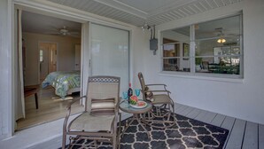 A covered patio with two wicker chairs, a small table with a watermelon and glasses, and a view of a room with a bed and a ceiling fan. - Peaceful Egret Pool Home in Venice (Venice)