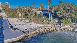 A coastal property with a paved walkway, lounge chairs, and a rocky shoreline. - Pass Key Rd Sandy Cove II (Siesta Key)