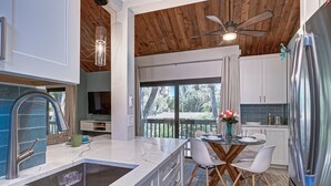 A modern kitchen with a large island, stainless steel appliances, and a dining area with a glass table and chairs. - Pass Key Rd Sandy Cove II (Siesta Key)