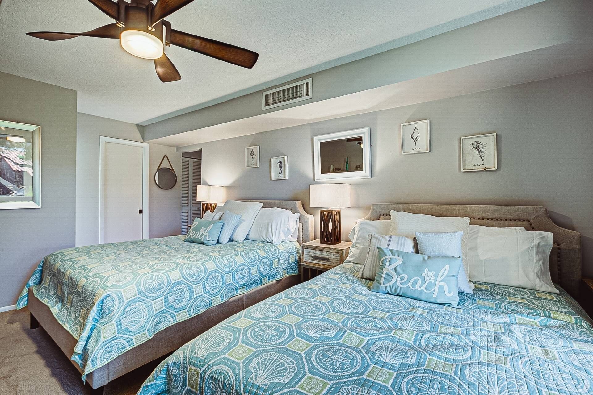 A bedroom with two beds, a ceiling fan, and framed artwork on the walls.