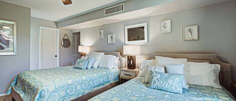 A bedroom with two beds, a ceiling fan, and framed artwork on the walls.