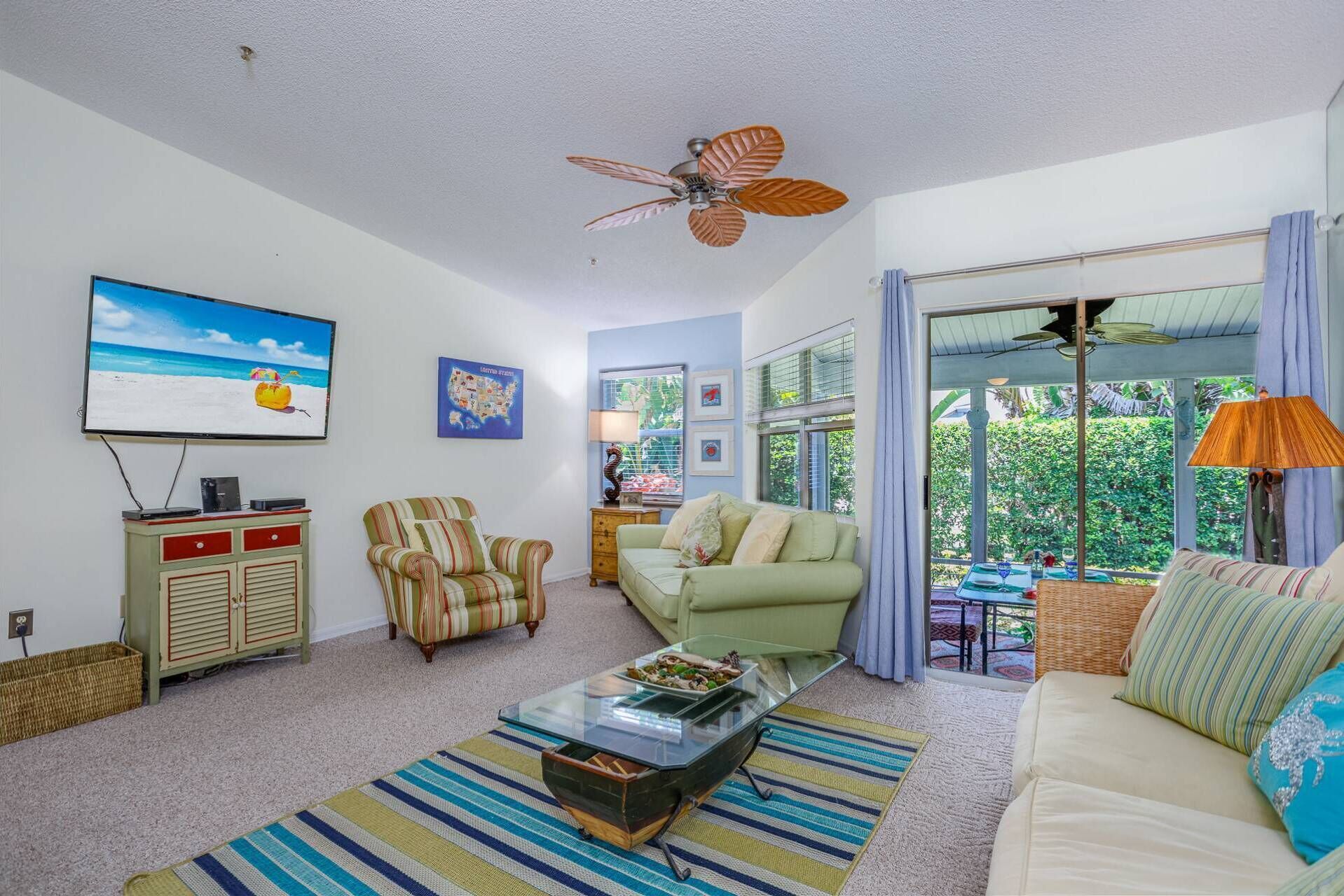 A living room with a ceiling fan, a television, a sofa, a striped armchair, and a coffee table.
