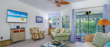 A living room with a ceiling fan, a television, a sofa, a striped armchair, and a coffee table.