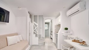 Un interior moderno con decoración blanca, que incluye un sofá, una mesa de comedor y una escalera que lleva a otra habitación.
