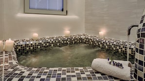 Un baño con bañera de azulejos, velas y una ventana.