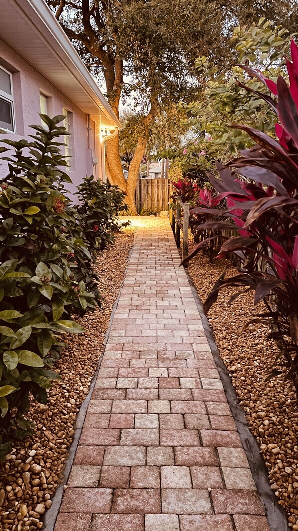 Un camino pavimentado que conduce a un edificio con una cerca de madera y árboles.