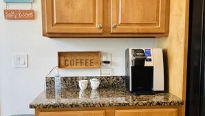 Une cuisine avec des meubles de rangement en bois, une machine à café et une poubelle.