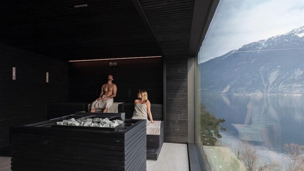 A modern spa with a large window overlooking a lake and mountains, a heated stone bath, and a seating area with a view. - Eala - My Lakeside Dream (Limone sul Garda)