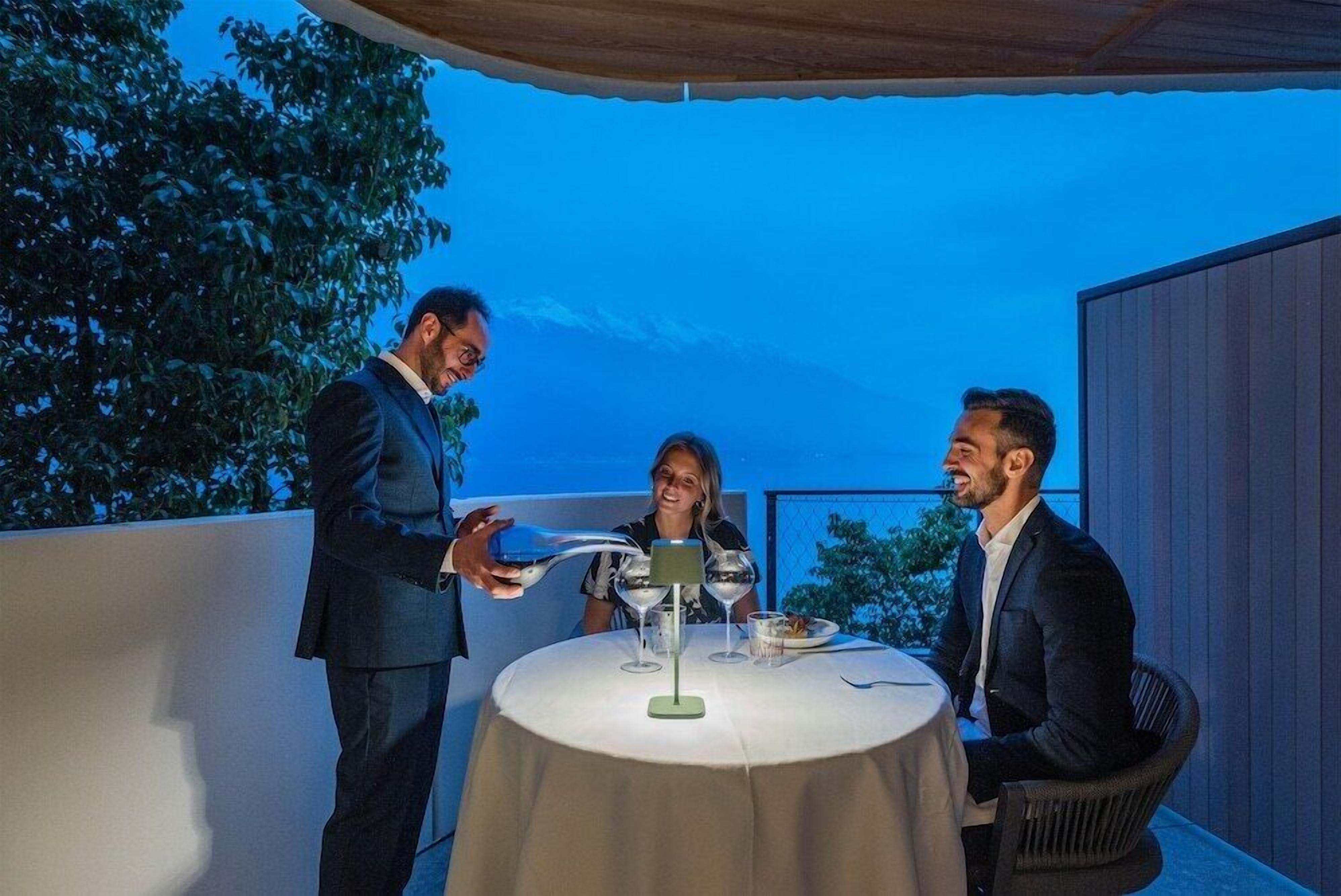 A table set outdoors with a tablecloth, a lamp, and a glass of water.