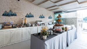 A buffet setup with a stone wall, decorative mountain art, and a variety of food items. - Melina Bay Boutique Hotel (Corfu)