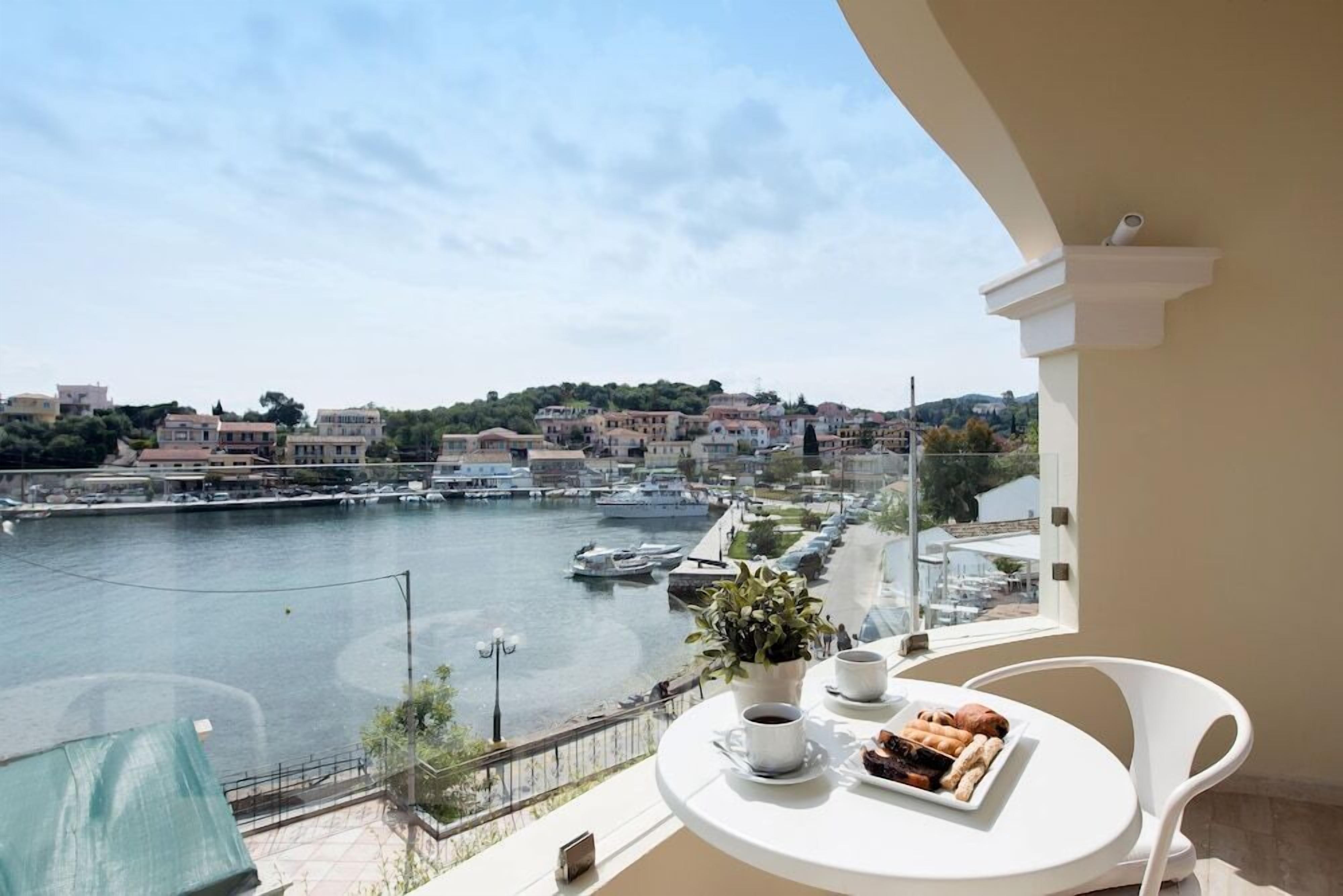 A balcony with a table set for two, overlooking a marina with boats and a cityscape.
