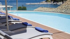 A poolside area with lounge chairs and towels, overlooking a clear blue pool and a rocky coastline. - Melina Bay Boutique Hotel (Corfu)