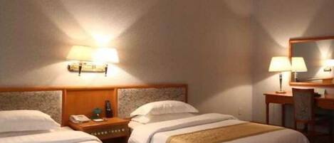 Une chambre d’hôtel avec deux lits, un bureau et une chaise. On y trouve des lampes fixées au mur et un miroir.