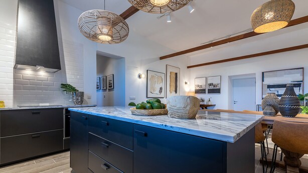 A modern kitchen with a marble countertop, dark cabinetry, and a large island. There are hanging wicker lights, a dining area with a wooden table, and various kitchen appliances. - Carregado House close to Lisbon (Carregado)