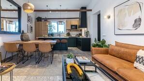 A modern living room with a brown sofa, a dining area with a wooden table and chairs, and a kitchen with dark cabinets and a large window. - Carregado House close to Lisbon (Carregado)