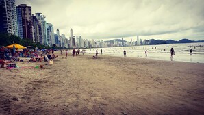Een strand met mensen, parasols en hoge gebouwen op de achtergrond.