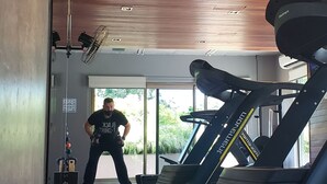Een sportschool met trainingsapparatuur, een rode rubberen vloer en houten plafondpanelen.