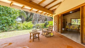 Une terrasse extérieure avec une table et des chaises en bois, entourée d’une végétation luxuriante et offrant une vue sur un jardin tropical.
